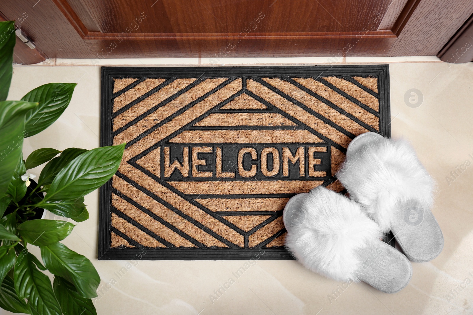 Photo of Welcome doormat and white slippers at door in hall, top view