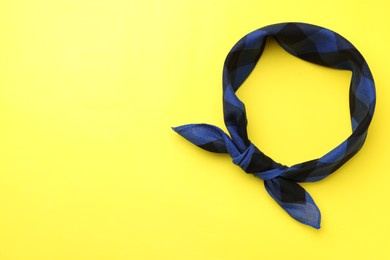 Tied blue checkered bandana on yellow background, top view. Space for text