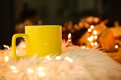 Photo of Yellow cup with hot drink and fairy lights on faux fur