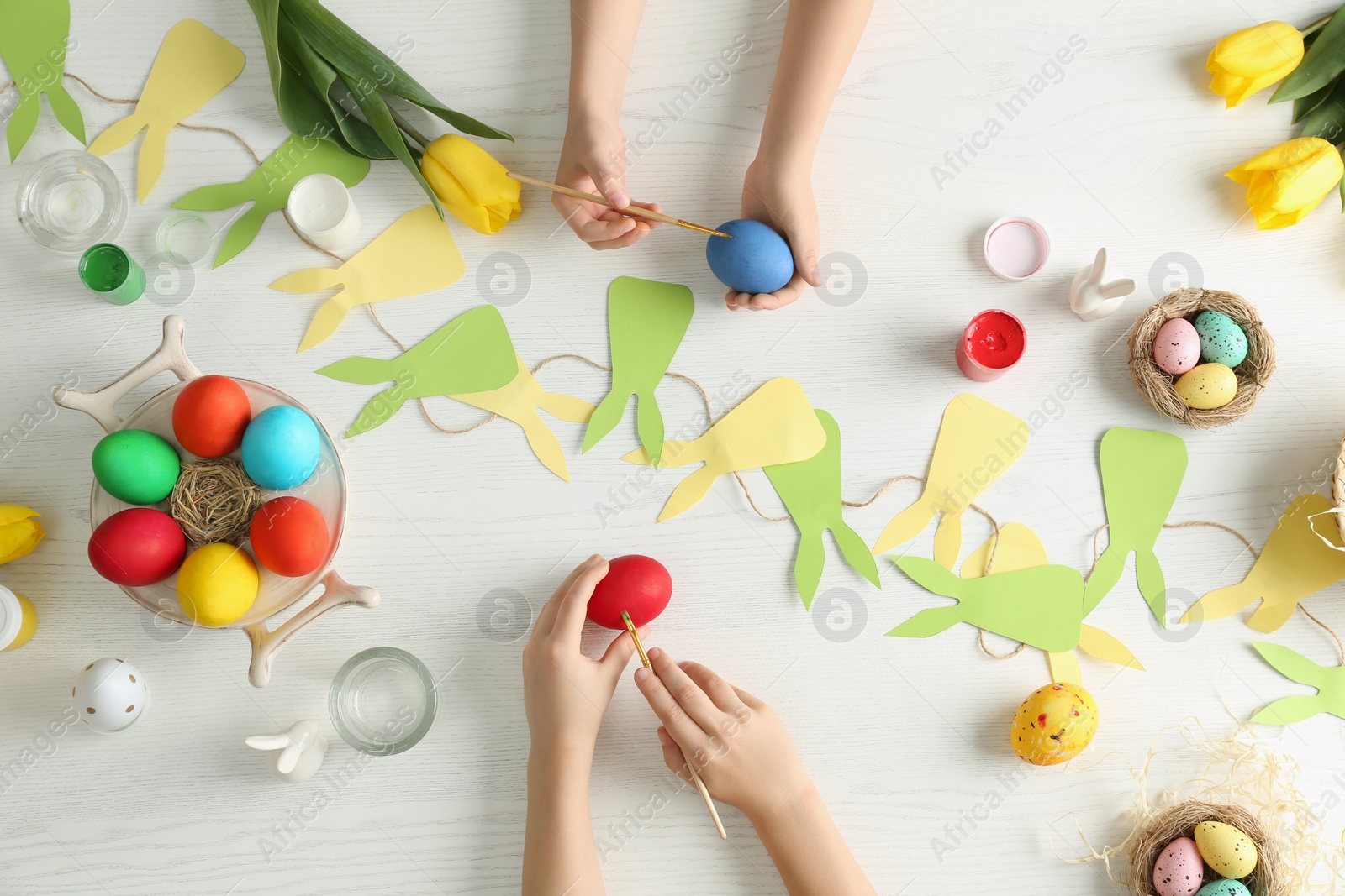 Photo of Little children painting Easter eggs at white wooden table, top view