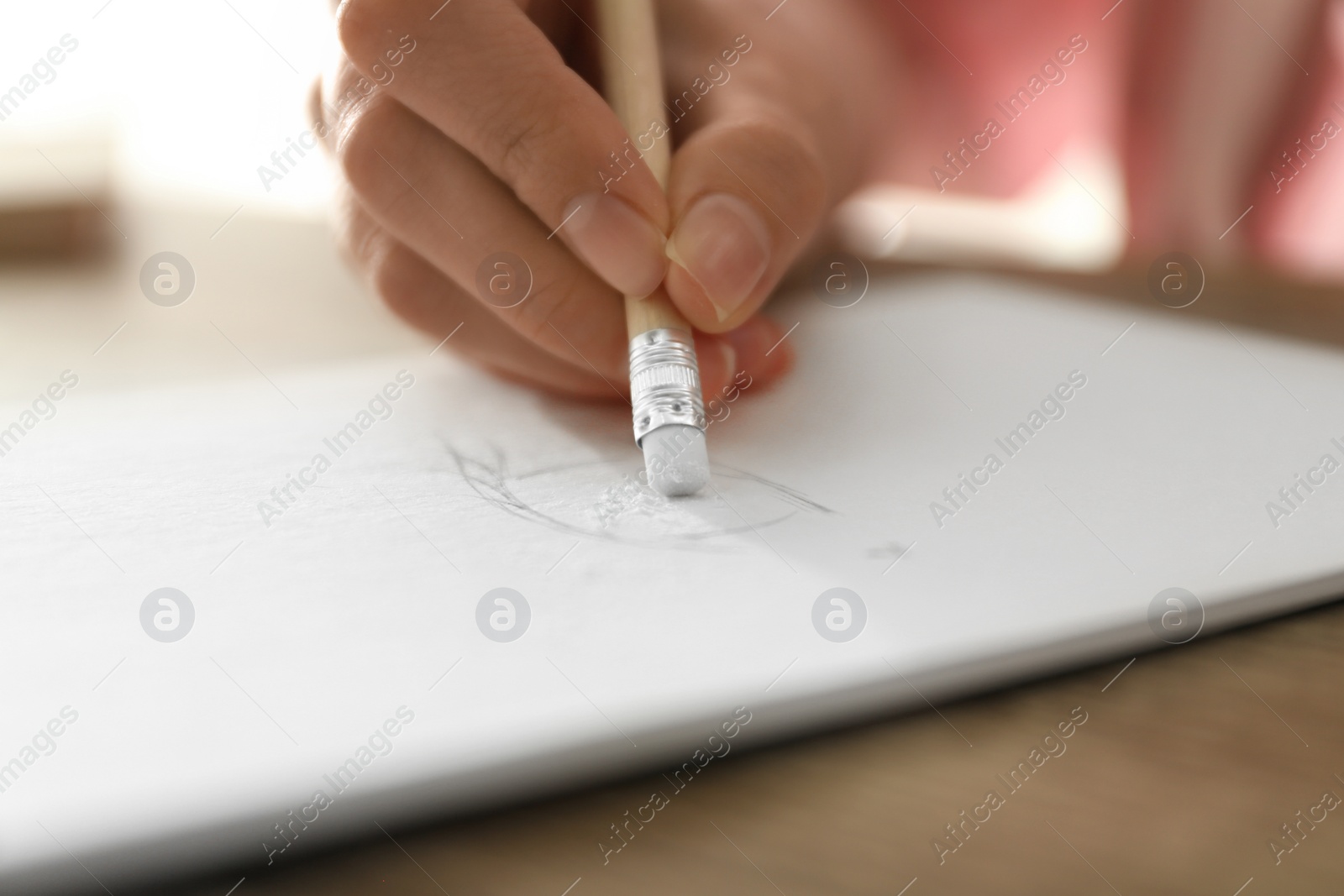 Photo of Woman correcting picture in notepad with pencil eraser at table, closeup