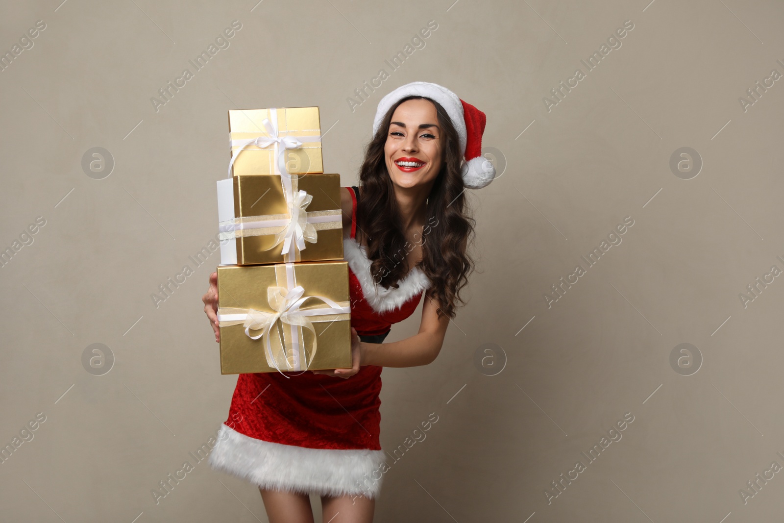 Photo of Beautiful woman in Christmas costume with gift boxes on beige background