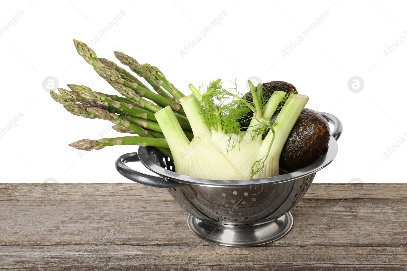 Photo of Metal colander with asparagus, fennel and avocados on wooden table against white background