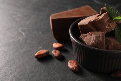 Pieces of tasty milk chocolate, mint and cocoa beans on black table, closeup. Space for text