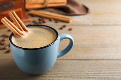 Photo of Cup of hot coffee with aromatic cinnamon on wooden table. Space for text