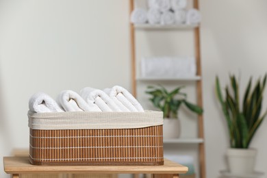 Photo of Wicker basket with folded soft terry towels on wooden table indoors, space for text
