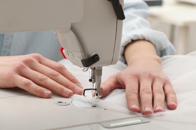 Photo of Dressmaker sewing new dress with machine in atelier, closeup
