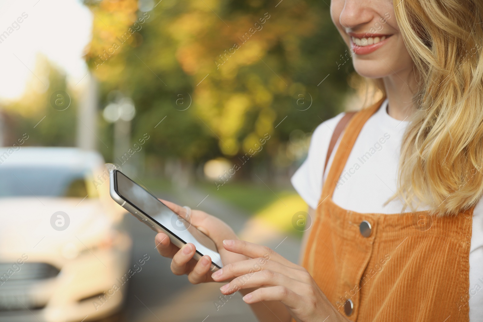 Photo of Woman ordering taxi with smartphone on city street, closeup