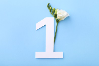 Paper number 1 and beautiful flower on light blue background, top view