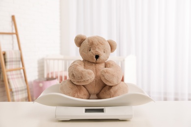 Photo of Baby scales with teddy bear on table in light room