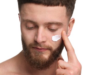 Handsome man applying moisturizing cream onto his face on white background