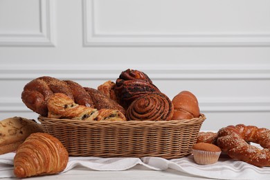 Photo of Wicker basket with different tasty freshly baked pastries on white wooden table