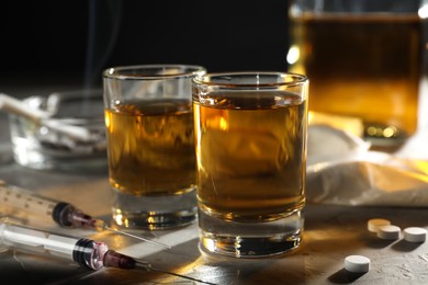 Alcohol and drug addiction. Whiskey in glasses, syringes and pills on grey background, closeup