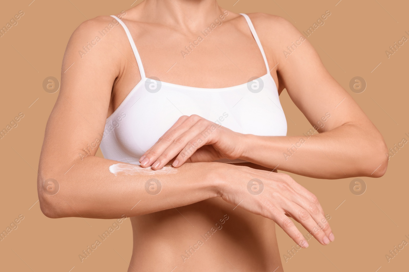 Photo of Woman applying body cream onto her arm against beige background, closeup