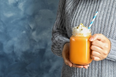 Photo of Woman in knitted sweater holding mason jar with pumpkin spice latte on color background. Space for text