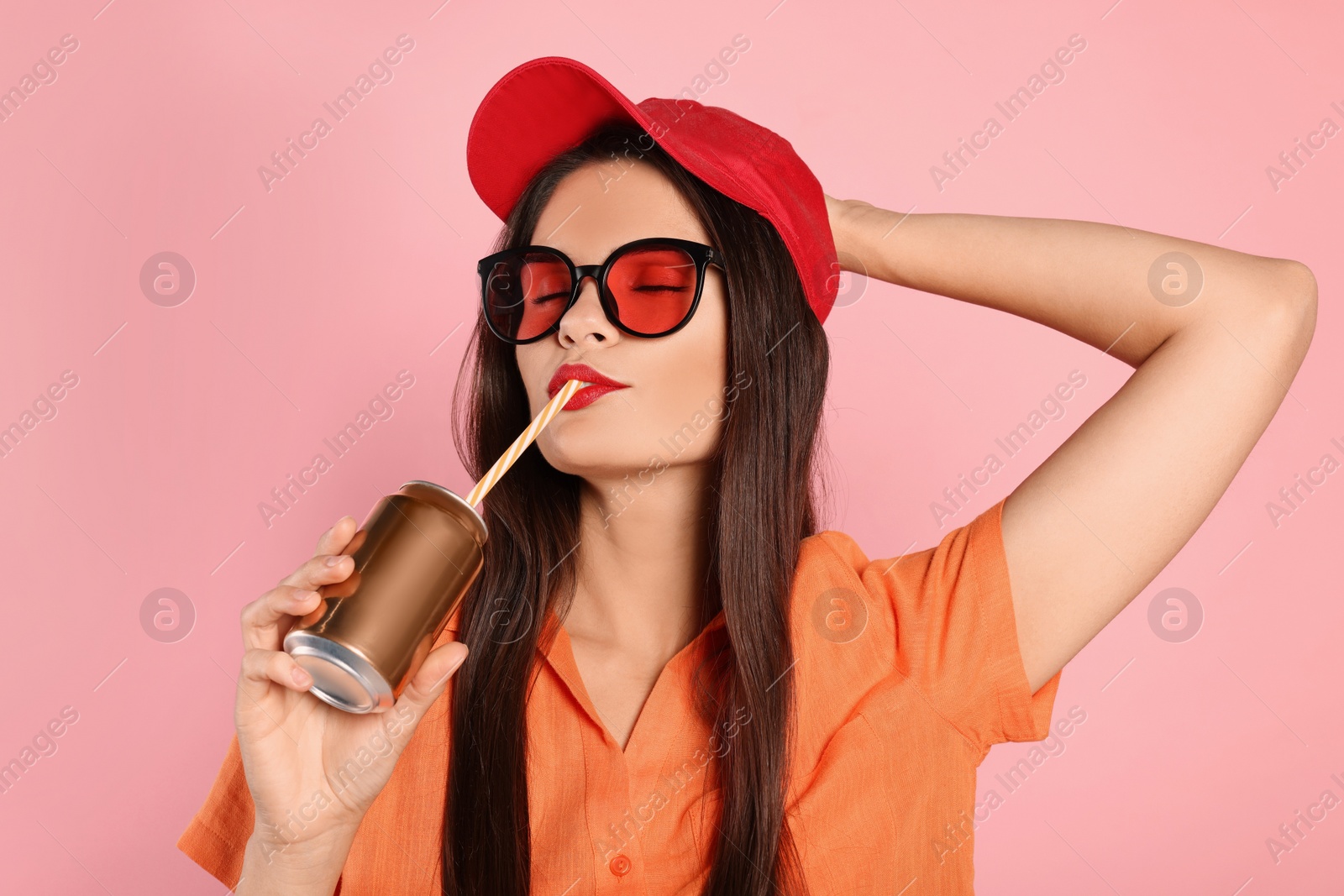 Photo of Beautiful young woman drinking from tin can on pink background