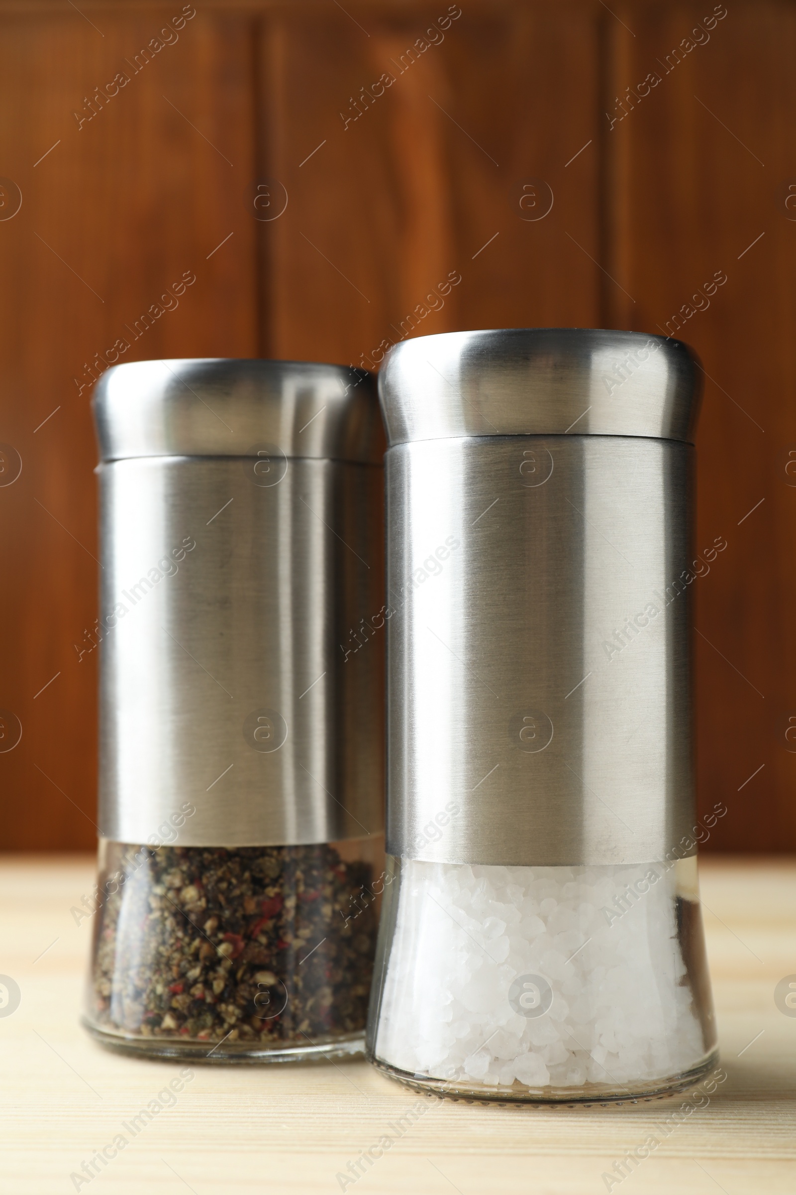 Photo of Salt and pepper shakers on light wooden table, closeup