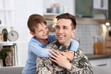 Photo of Young man in military uniform with his little son at home
