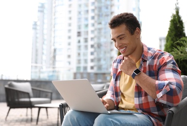 Photo of Portrait of handsome young African-American man with laptop in outdoor cafe