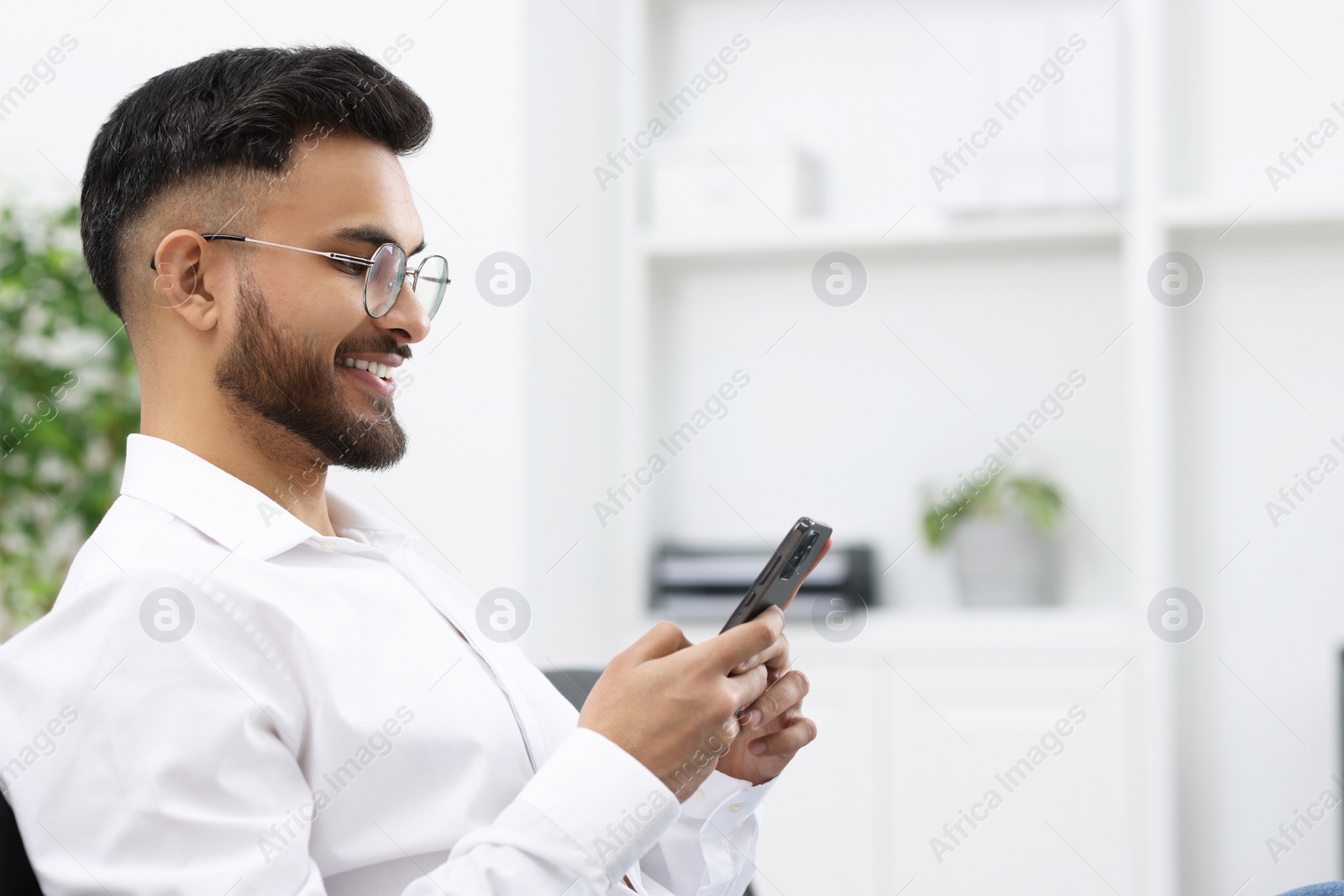 Photo of Happy young man using smartphone in office, space for text