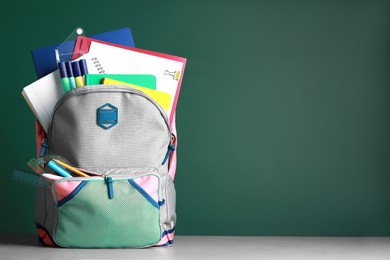Backpack with different school stationery on white table near chalkboard, space for text