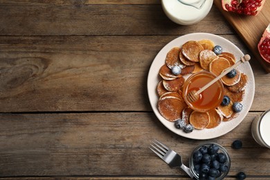 Photo of Delicious mini pancakes cereal with blueberries and honey served on wooden table, flat lay. Space for text