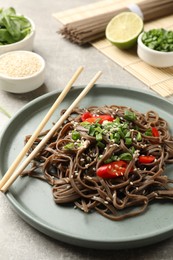 Photo of Tasty buckwheat noodles (soba) with chili pepper, onion and chopsticks on light table, closeup