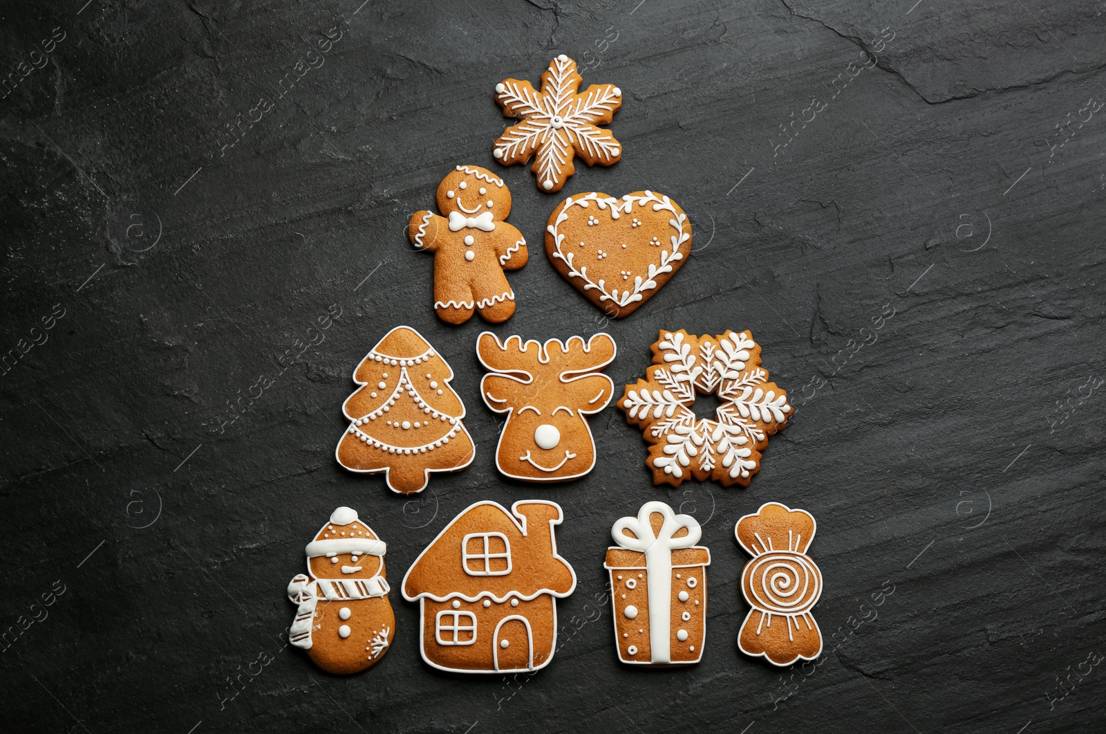 Photo of Christmas tree shape made of delicious decorated gingerbread cookies on black table, flat lay