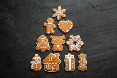 Photo of Christmas tree shape made of delicious decorated gingerbread cookies on black table, flat lay