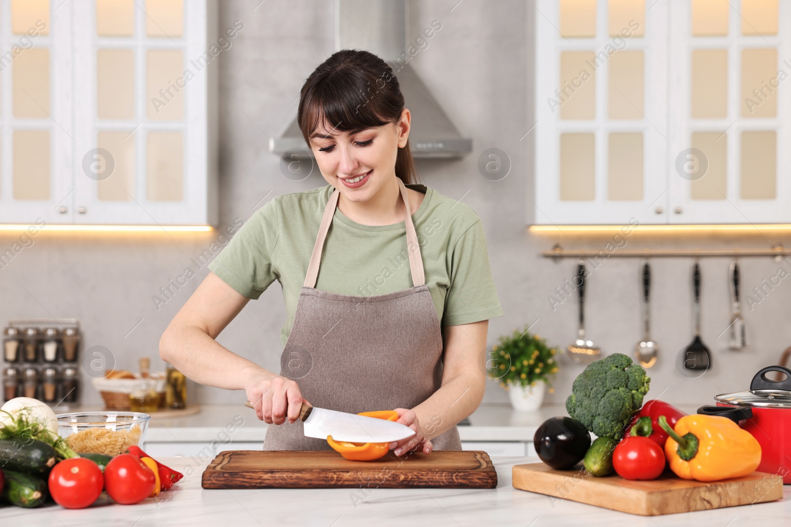 Photo of Happy young housewife cutting bell pepper at white marble table in kitchen