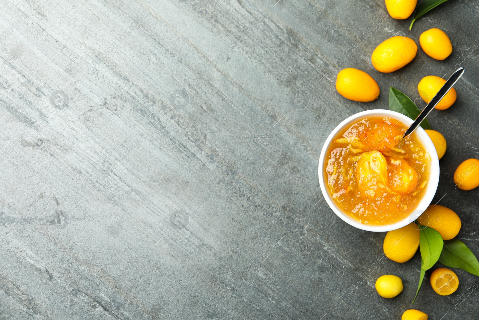 Photo of Delicious kumquat jam in bowl and fresh fruits on grey table, flat lay. Space for text