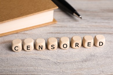 Photo of Cubes with word Censored, notebook and pen on wooden table, closeup