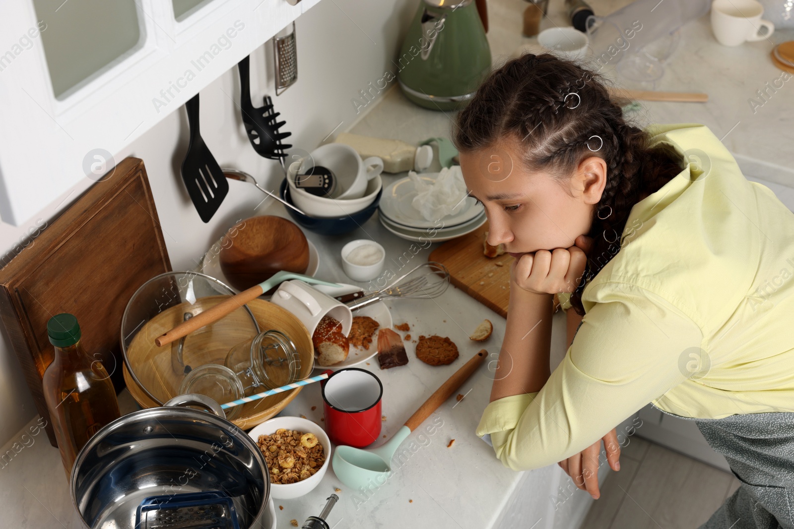 Photo of Stressed woman leaning on countertop with many dirty dishware, utensils and food leftovers. Mess in kitchen