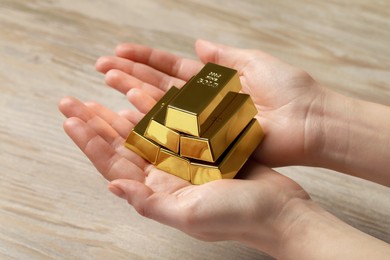 Photo of Woman holding gold bars at wooden table, closeup