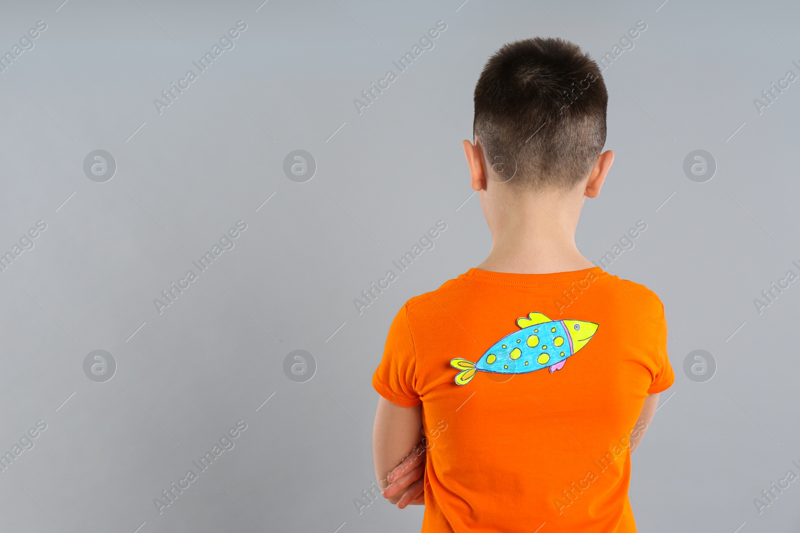Photo of Preteen boy with paper fish on back against light grey background, space for text. April fool's day