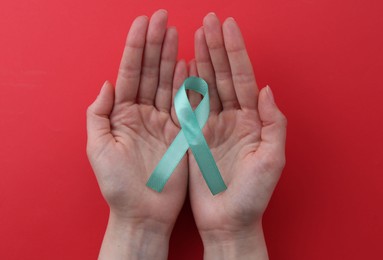 Photo of Woman holding turquoise awareness ribbon on red background, top view