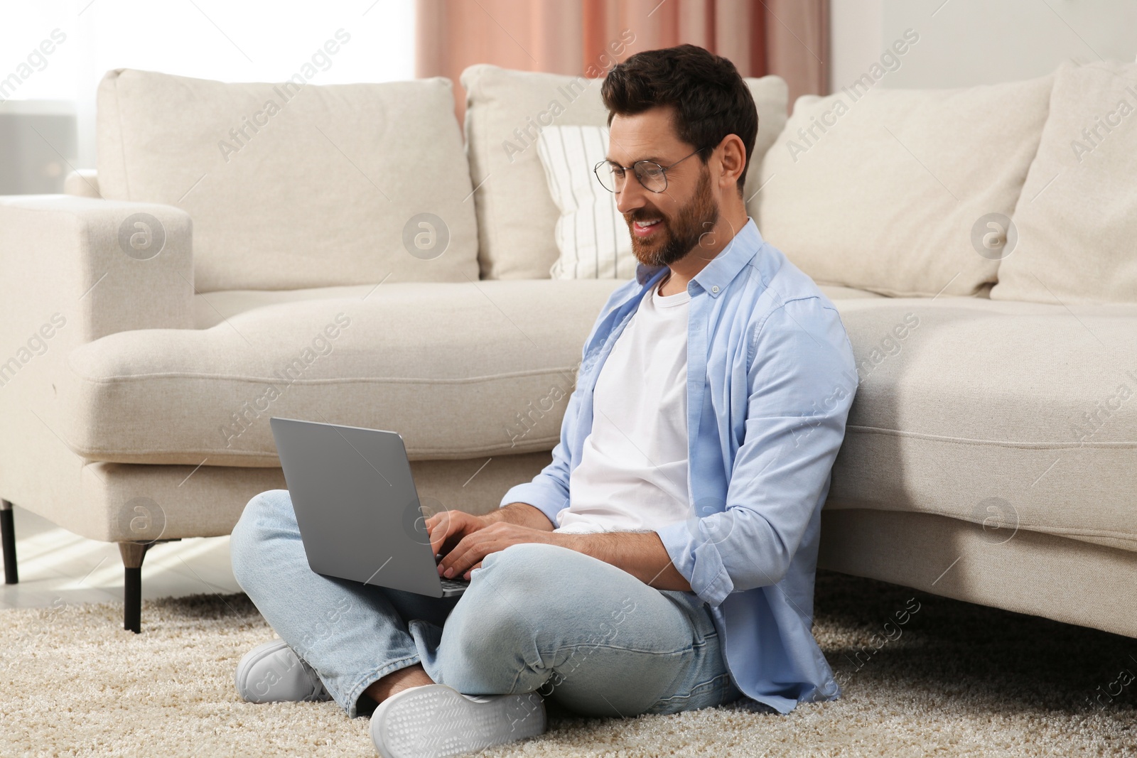 Photo of Man using laptop on floor near sofa at home