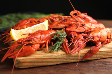 Delicious boiled crayfishes with lemon and dill on wooden table, closeup