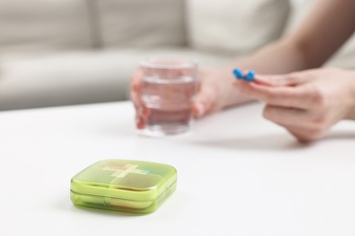 Photo of Woman with pills, organizer and glass of water at white table, selective focus