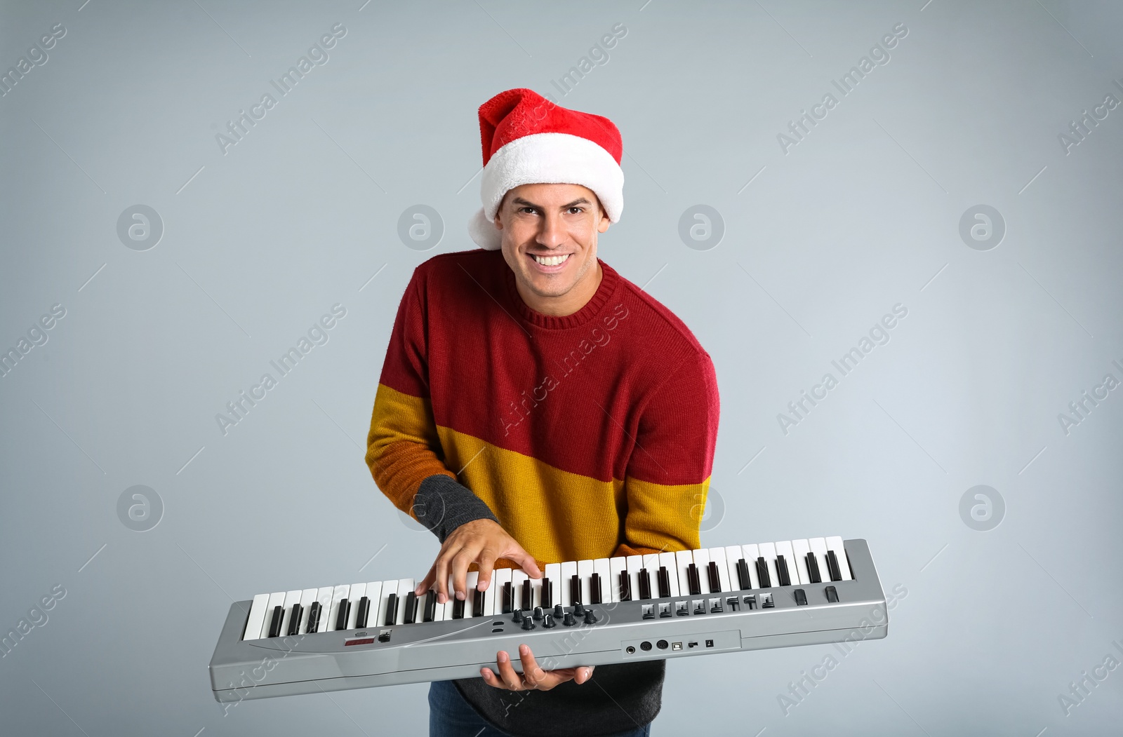 Photo of Man in Santa hat playing synthesizer on light grey background. Christmas music