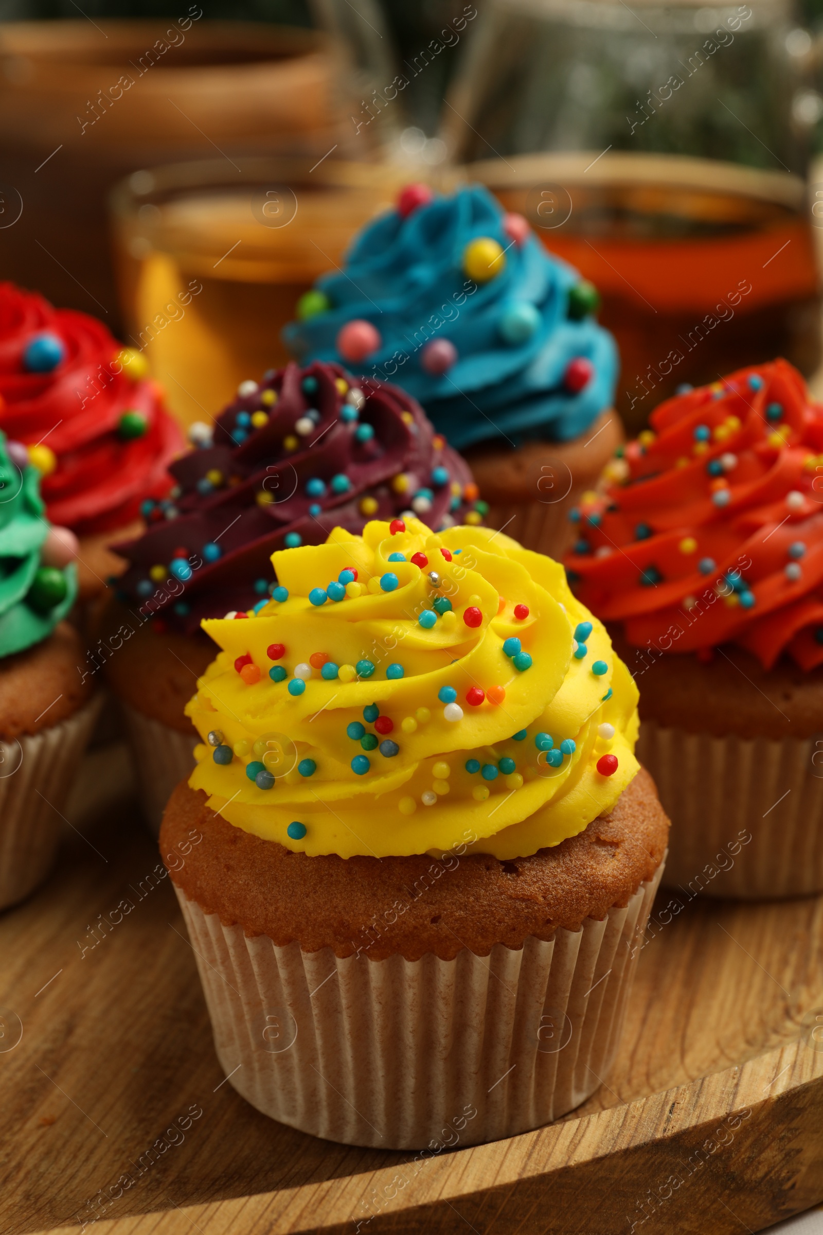 Photo of Delicious cupcakes with colorful cream and sprinkles on wooden board, closeup