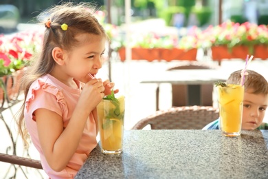 Photo of Cute children with natural lemonade at table in cafe