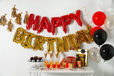 Treats and gifts on table in room decorated for birthday party with different balloons