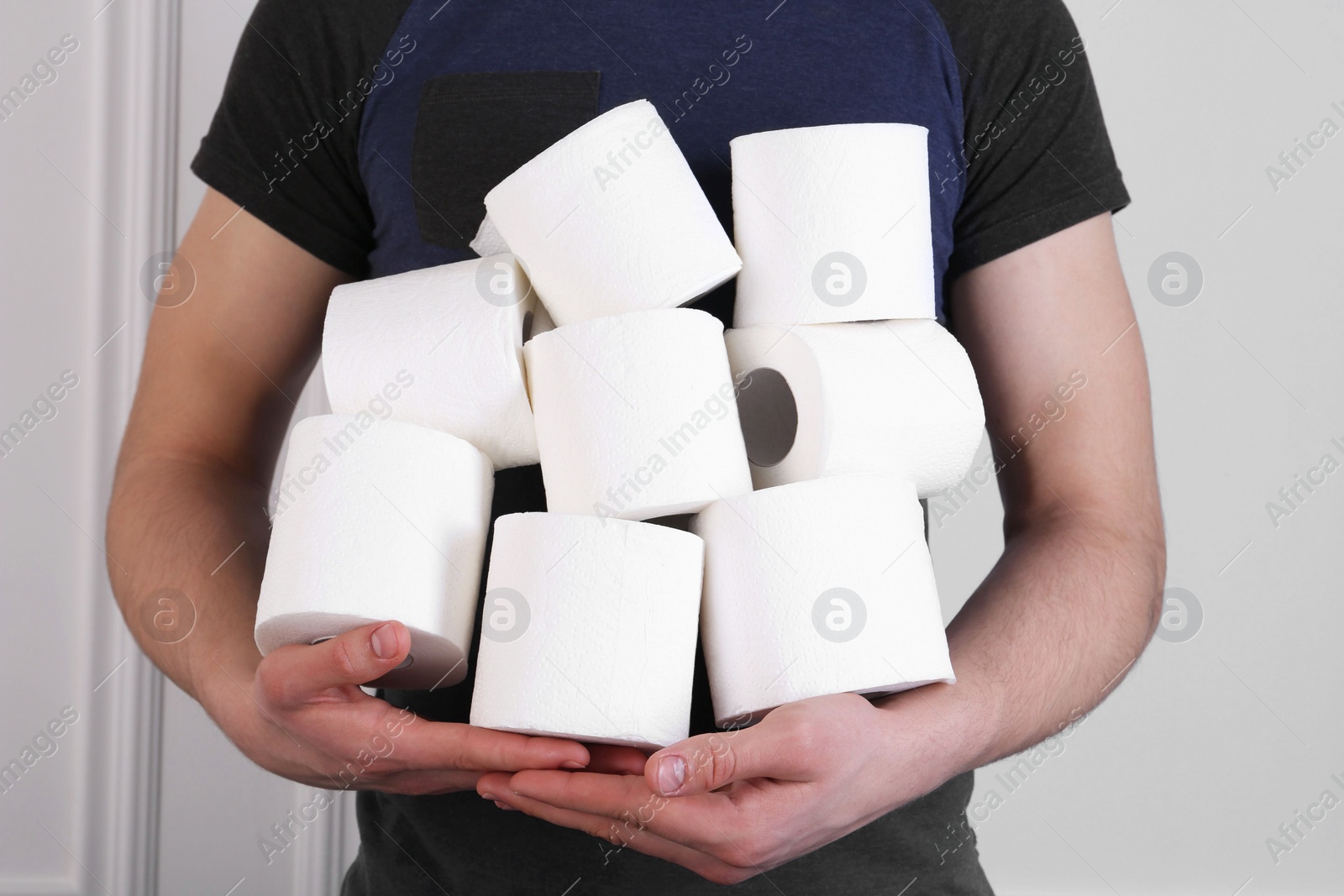 Photo of Man with many toilet paper rolls near white wall, closeup