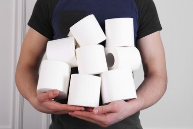 Photo of Man with many toilet paper rolls near white wall, closeup