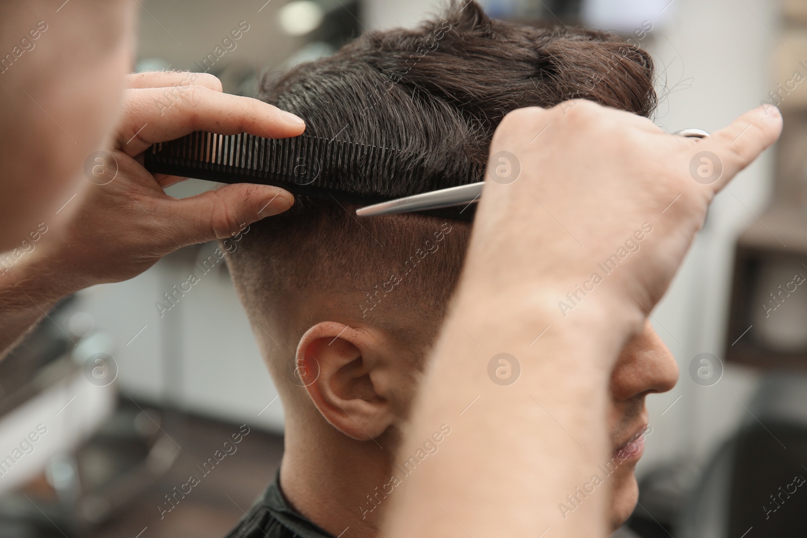 Photo of Professional barber making stylish haircut in salon, closeup