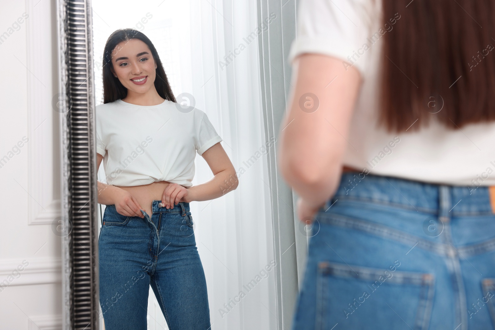 Photo of Young woman in stylish jeans near mirror indoors