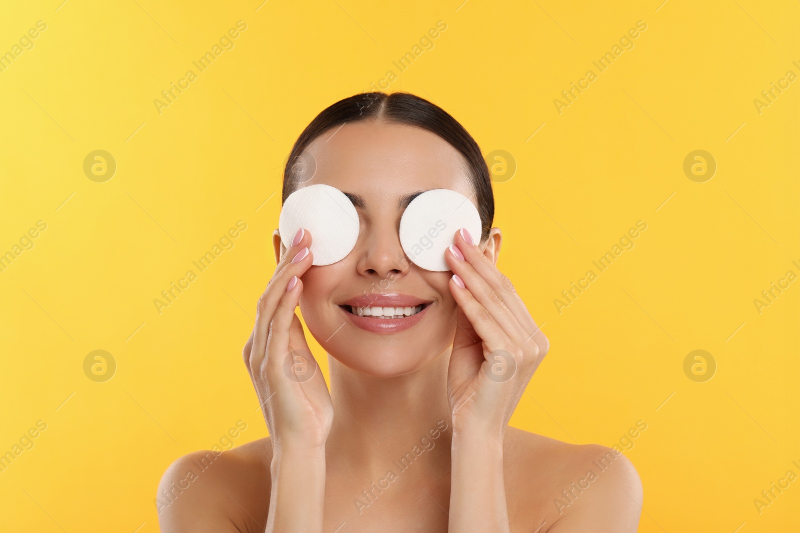 Photo of Beautiful woman removing makeup with cotton pads on yellow background