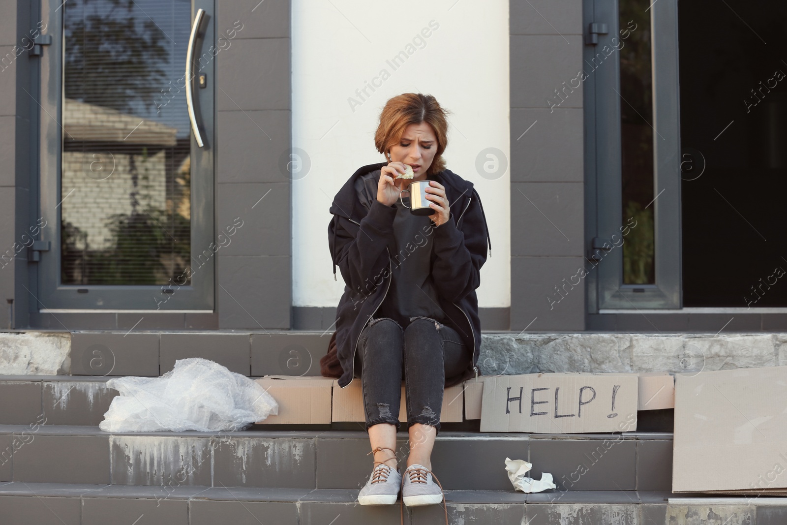 Photo of Poor woman with piece of bread and mug on city street