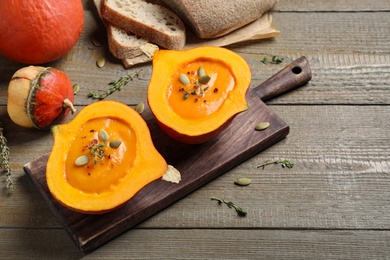 Photo of Tasty cream soup in pumpkin halves on wooden table